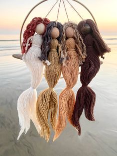 several different colored tassels hanging from a wooden hoop on the beach with water in the background