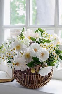 a wicker basket filled with white flowers next to a book on a window sill