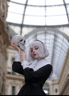 a woman with white hair holding a skull in her hand while wearing a black dress