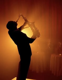 a man is playing the saxophone in front of a light that is shining down on him