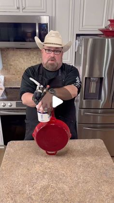 a man in a cowboy hat is pouring something into a red pot on a counter