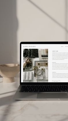 an open laptop computer sitting on top of a white table next to a wooden bowl