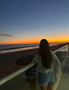 a woman is looking out over the beach at sunset