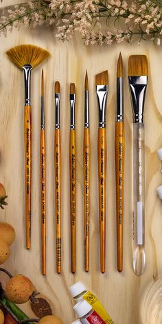 the brushes are lined up next to each other on top of a wooden table with fruit and flowers