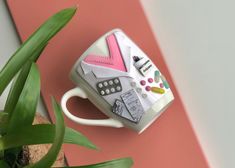 a coffee cup that is sitting on top of a pink table next to a potted plant