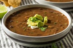 two white bowls filled with soup and garnished with avocado