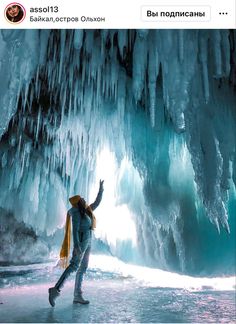 a woman is standing in front of an ice cave and pointing at the light coming through it