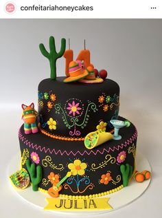 a black cake decorated with colorful decorations and cactuses on the top is for julia's 1st birthday