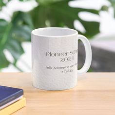 a white coffee mug sitting on top of a wooden table next to a blue book