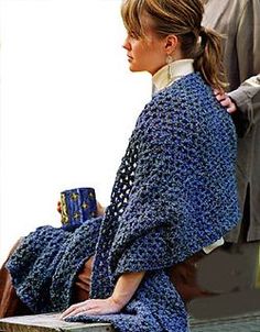 a woman in a blue crocheted shawl sitting on a bench