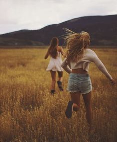 two young women running through a field with tall grass