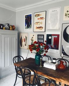 a dining room table with chairs and pictures on the wall above it, along with vases filled with flowers