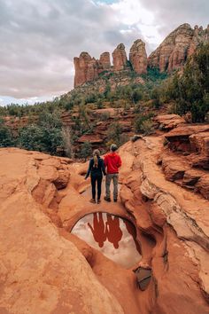 two people are standing on the edge of a rock formation with water in its hole