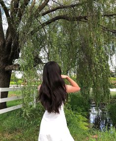 a woman standing in front of a tree with her back to the camera and looking at water