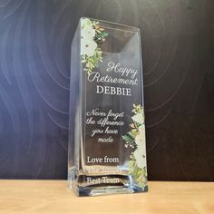 a clear glass award with flowers on the front and bottom, says happy retirement debie