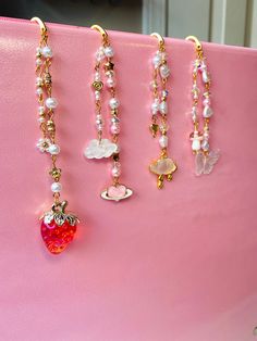 three necklaces hanging from a pink purse with pearls and charms attached to the handles