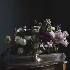 a vase filled with lots of flowers on top of a wooden table next to a wall