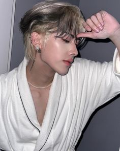 a woman with blonde hair wearing a white shirt and black pants holding her hand up to her head