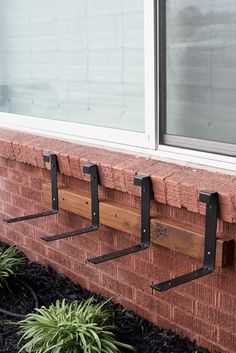 three coat hooks are attached to the side of a brick building with plants in front