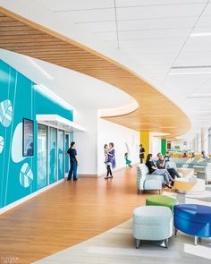 people are standing and sitting in the waiting area of an airport lobby with blue walls