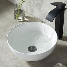 a white bowl sink sitting under a faucet next to a black faucet