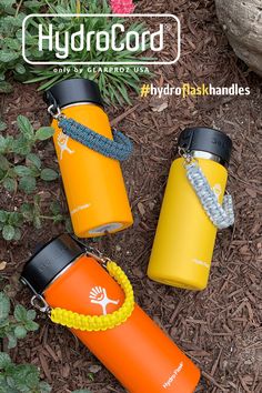 three hydro flasks sitting on the ground in front of flowers and plants, one with a lanyard around it