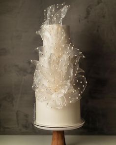 a three tiered white wedding cake decorated with pearls and ribbons on a wooden stand