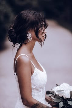 a woman in a white dress holding a bouquet of flowers and looking off into the distance