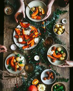 people are sitting at a table with bowls of food and plates of fruit on the table