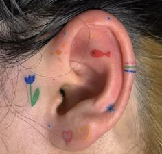 a person with colorful tattoos on their ear and behind the ear is a fish, flowers, and hearts