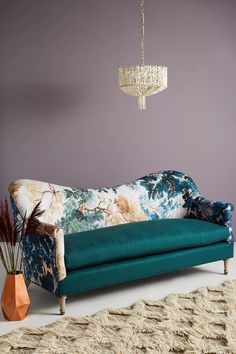 a blue couch sitting next to a vase with flowers on it and a chandelier hanging from the ceiling