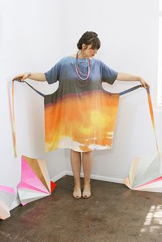 a woman standing in front of a wall holding onto two kites that look like they have been made out of paper