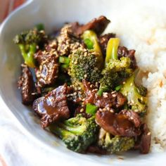 a white bowl filled with rice and broccoli covered in sauce on top of a table