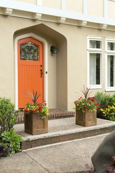 an orange front door with two planters on the steps