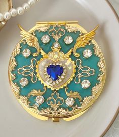 a blue heart shaped brooch sitting on top of a white plate next to pearls