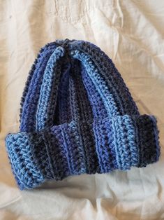 a blue and gray knitted hat laying on top of a white bed sheet,