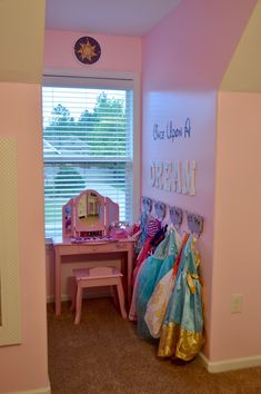 there is a pink room with clothes hanging on the wall and a small desk in front of it