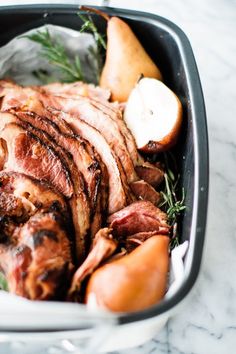 a roasting pan filled with meat, potatoes and apples on top of a marble counter