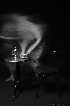 a black and white photo of a chair next to a table with a teapot on it