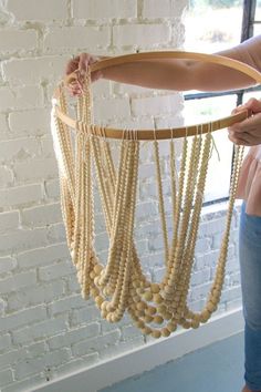 a woman is holding a large wooden bead mobile in front of a brick wall