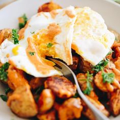 a white plate topped with fried potatoes and an egg on top of it, next to a fork