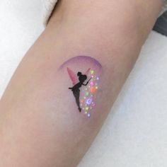 a small tattoo on the arm of a woman with a pink and green fairy duster