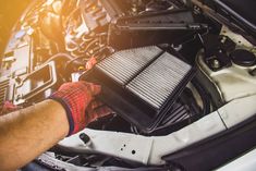 a man is working on an engine in his car, with the hood up and it's air filter removed