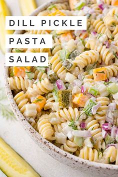 a bowl filled with pasta salad on top of a white table next to yellow and green vegetables