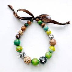 this necklace is a shorter version of the long domino necklace that was inspired by the 2007 India Hicks cover of Domino magazine. a bold statement piece to elevate your everyday style - wooden beads in with animal prints and deep greens in an unexpected mix and strung on a coordinating ribbon.the strand of beads measures 17" in length but the ribbon makes it easy to wear it as long or as short as you'd like.Please Note:* your piece may vary slightly from the one shown - while the colors and pro India Hicks, Domino Magazine, Hand Painted Necklace, Ways To Get Money, Wooden Bead Necklaces, Needlepoint Designs, How To Make Ribbon, Animal Prints, Deep Green