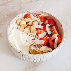 a bowl filled with fruit and nuts on top of a white countertop next to a spoon