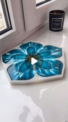 a blue flower on a white counter top next to a candle and window sill