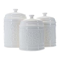 three white canisters with decorative designs on the top and bottom, one has a lid