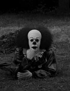 a creepy clown sitting in the grass