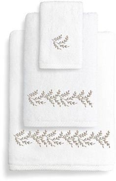 three white towels with embroidered leaves on the front and bottom, one in gold foil